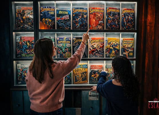 Zwei Frauen wählen ein Superhelden-Comic aus einem Regal im Escape Room.